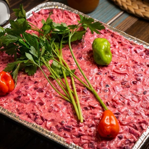 A vibrant pink beet salad in a foil tray, garnished with fresh parsley and small peppers.