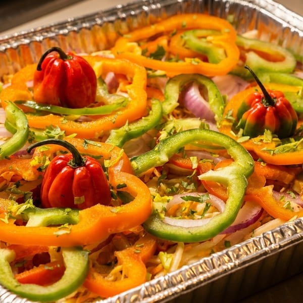 Colorful bell peppers, red onions, and habanero peppers garnish a dish in a foil pan.